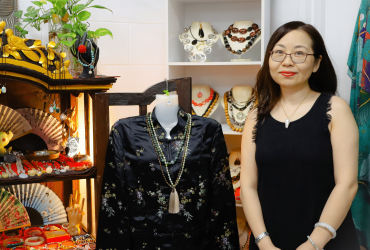 Jinglin standing in her store with some jewellery, fans and clothing