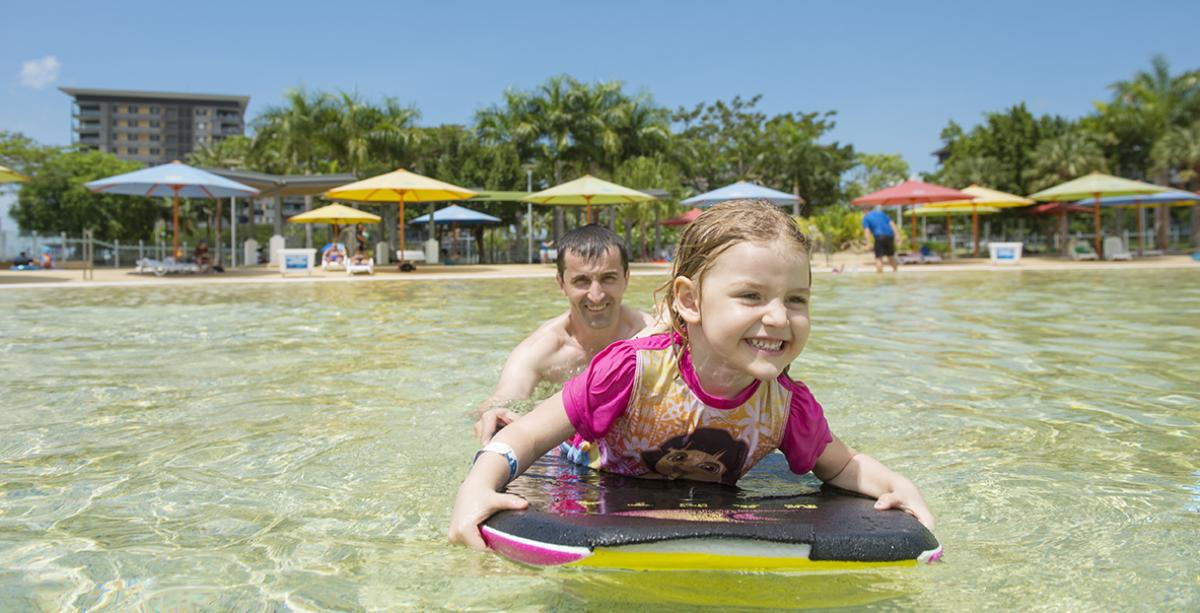 Young girl on paddle board while Dad pushes her through the water