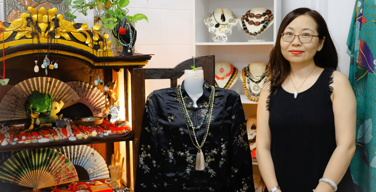 Jinglin standing in her store with some jewellery, fans and clothing