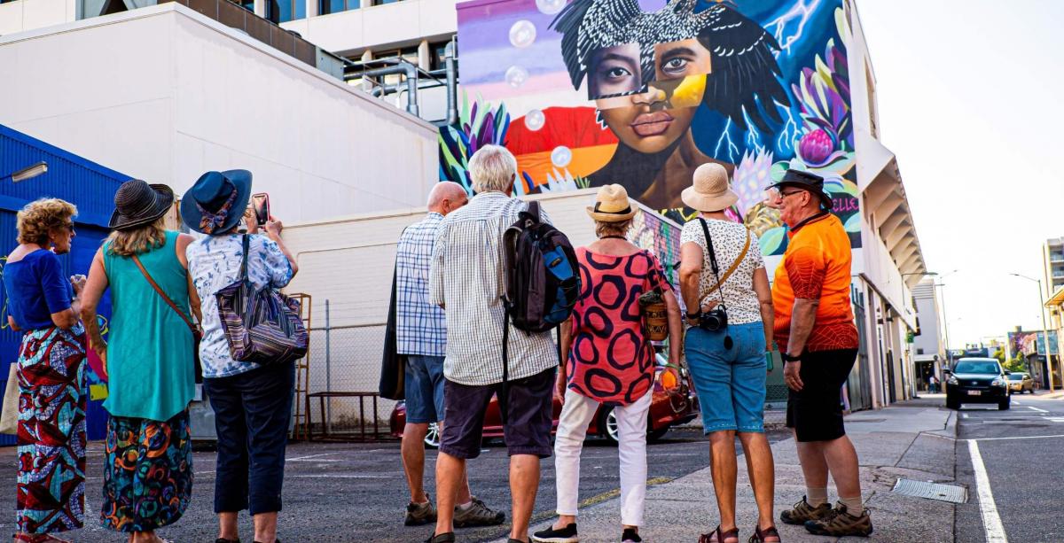 Walk Darwin tour guide talking to group of tourists with street art mural in background